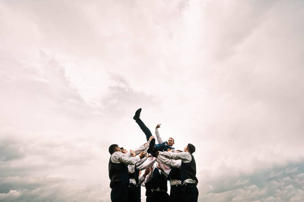 groom being tossed into the air by groomsmen by Roy Serafin Photo Company