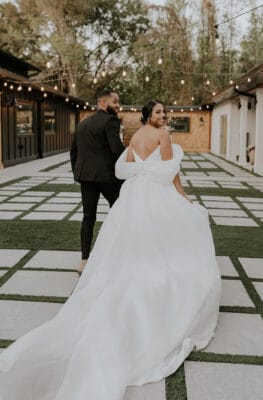 bride in gown from Theory Bridal House and groom walking on cement stepping stones under market lights at Theory Bridal House