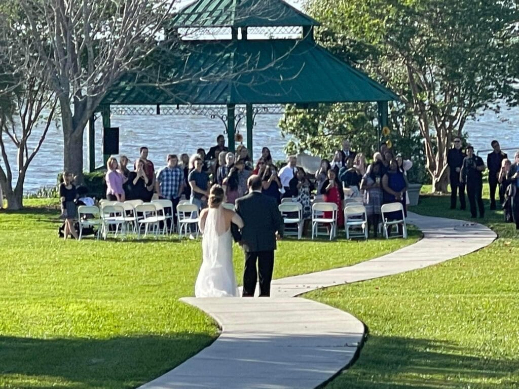 bride walking with her escort down path to wedding pavilion by the lake