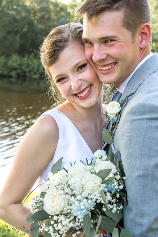 groom in dusty blue suit hugging bride with white floral bouquet by Petals and Stems Market