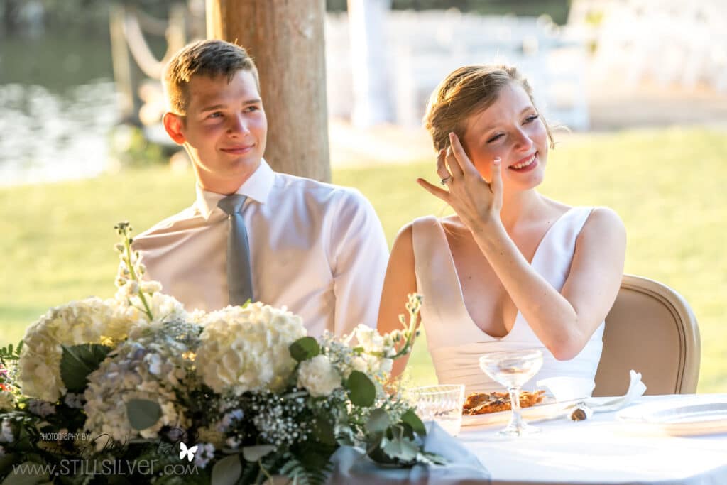 bride and groom sitting at sweetheart table with water in the background and centerpiece by Petals and Stems Market