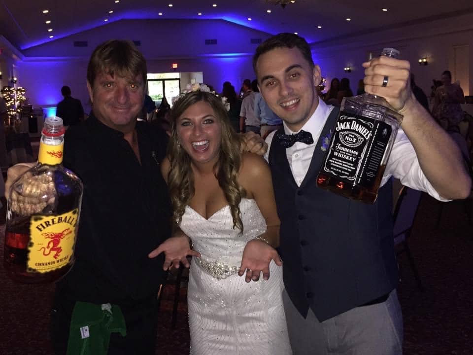 bride, groom and bartender posing with liquor bottles and enjoying the moment....