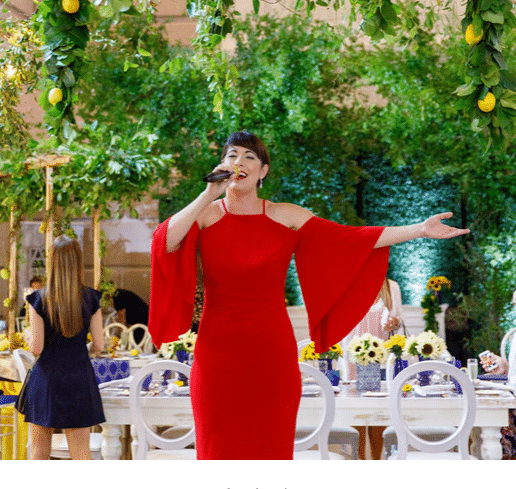 a woman from Dawn Gilmore Productions performing in a red dress in a room draped wit greenery