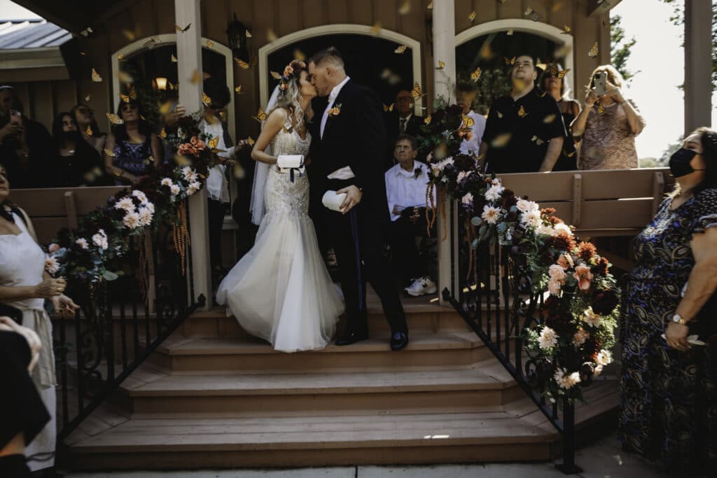 bride and groom kissing on steps of aisle with pew end flowers by Petals and Stems Market