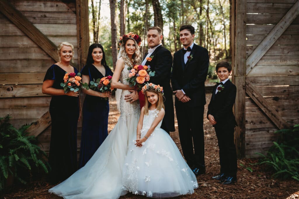 wedding party in the woods against wooden doors with orange and rust bouquets by Petals and Stems Market
