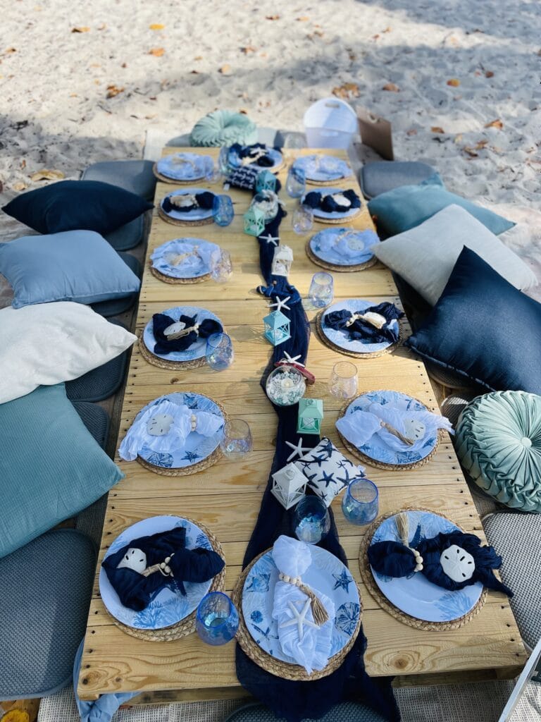Reception set up by the sea. The plates are nautical themed with pillows for sitting and a palette table