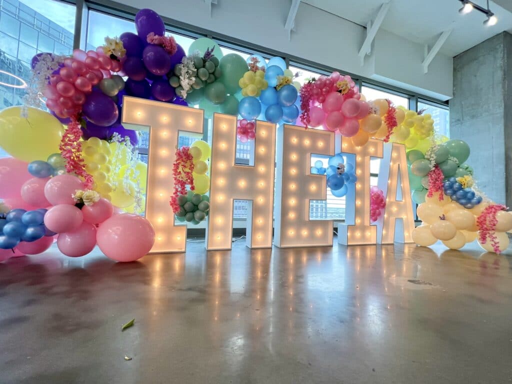 rainbow of colorful balloons with name in white lights and large letters by Fab and Float events