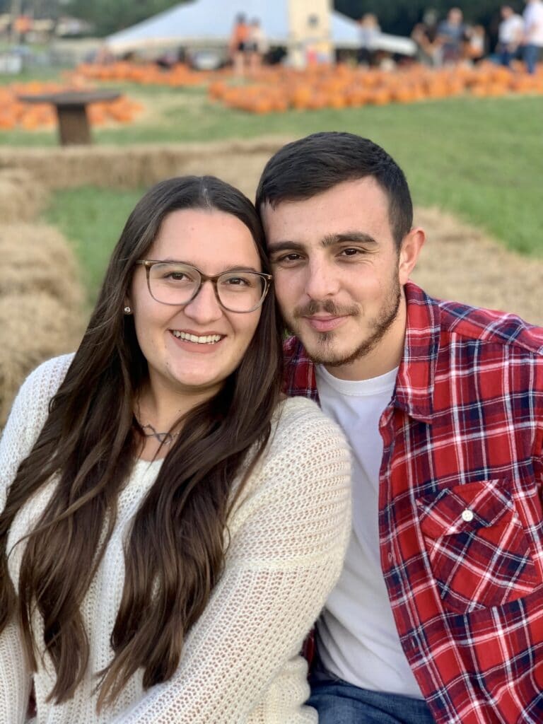 man in plaid shirt posing with his girlfriend in a pumpkin patch