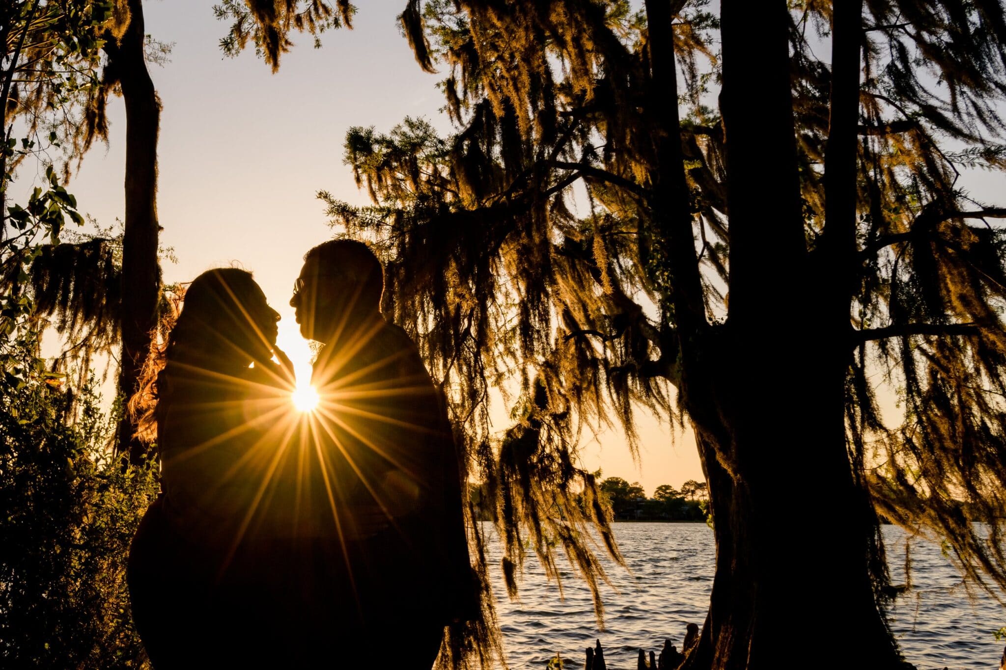 couple silhouetted at sunset by the lake with trees and Spanish moss