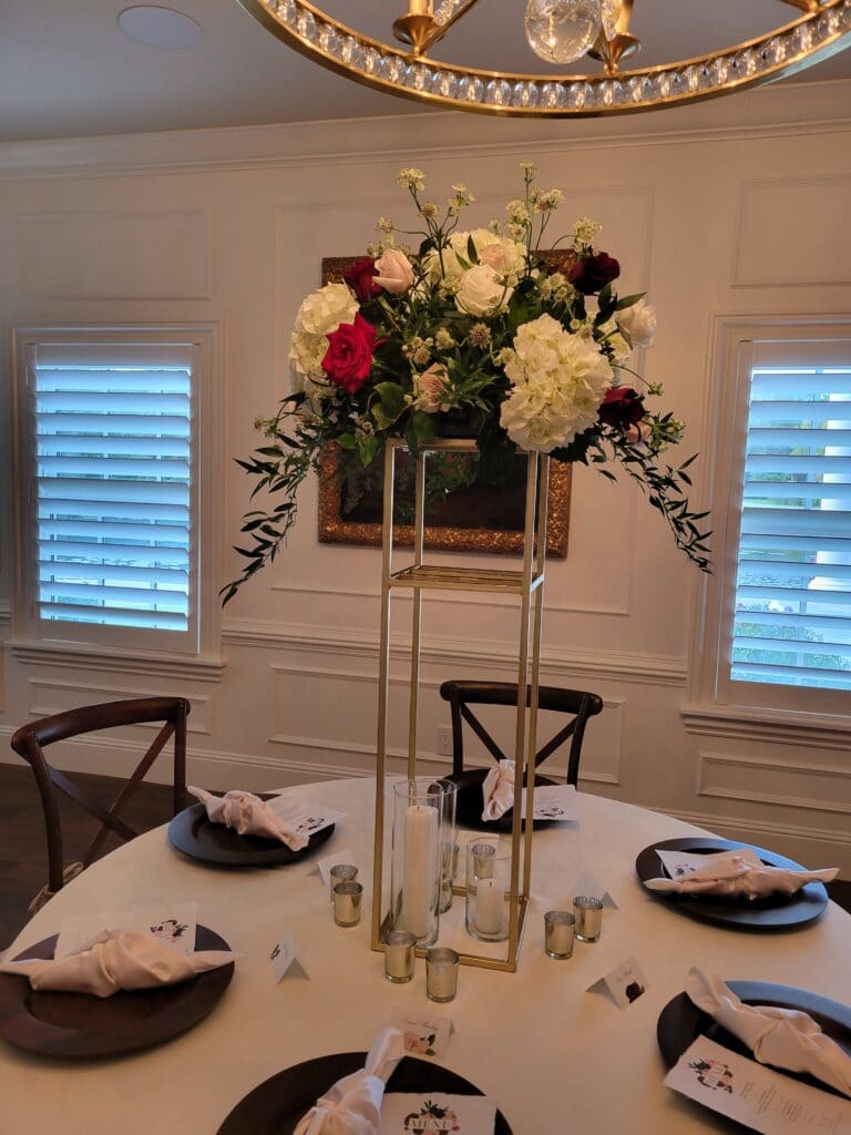 Tall centerpiece with flowers. The table is decorated with menus, tableware, and place cards.