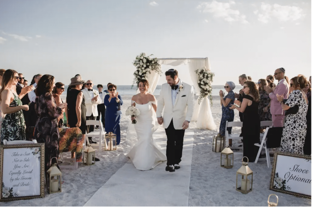 bride and groom walk down aisle at beach with florals by Petals and Stems Market