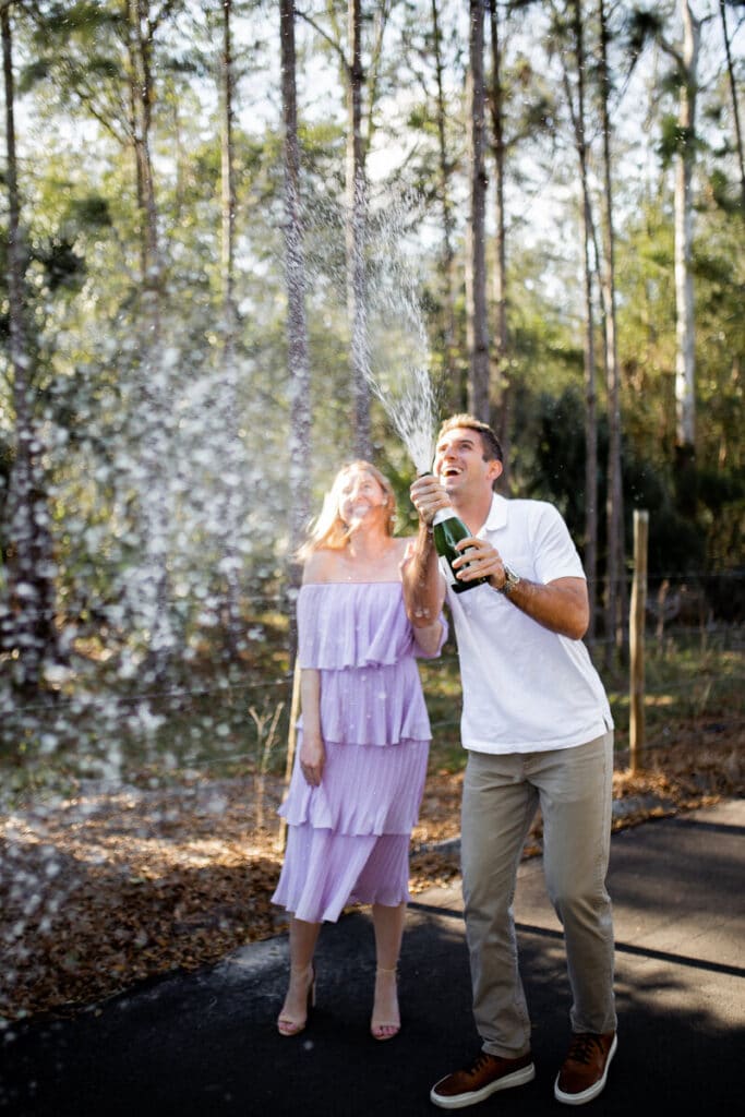 woman in lavender dress and man in khakis celebrate with champagne at The Black Barn