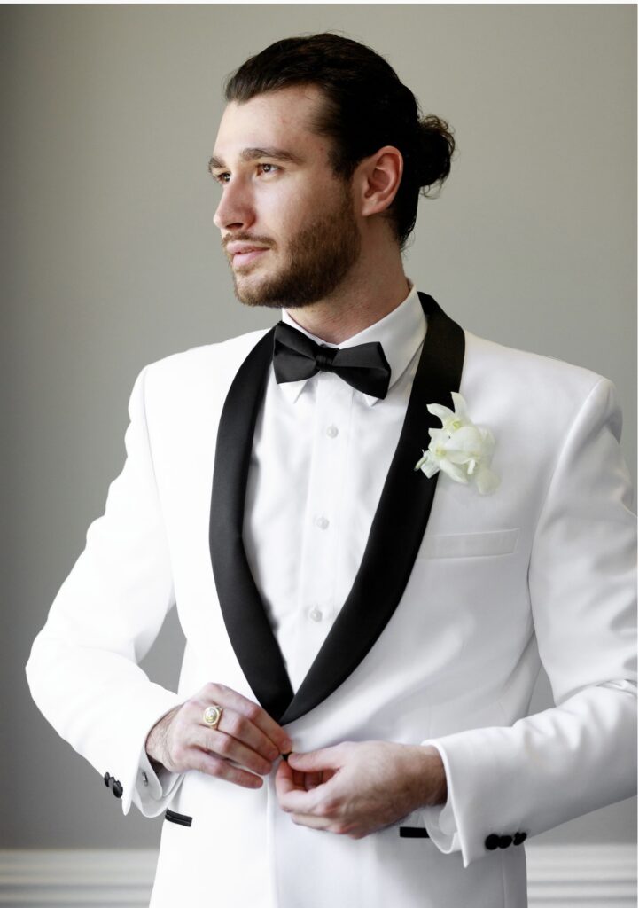 groom with man bun in white tuxedo jacket with black lapels and black bow tie from the Ivy Bridal Shop