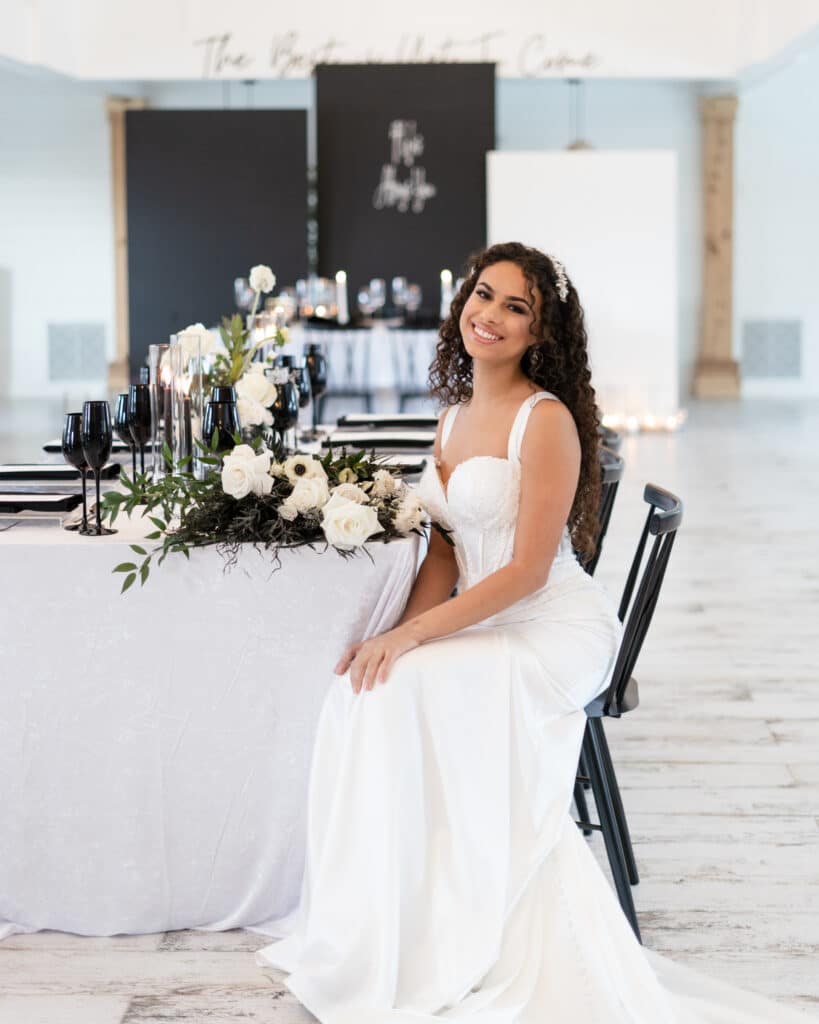 bride sitting at reception table with white tablecloths and black chairs and accents at The Black Barn