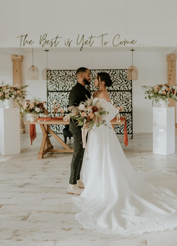 bride and groom embracing in a white room with 'the best is yet to come' sign behind them at The Black Barn