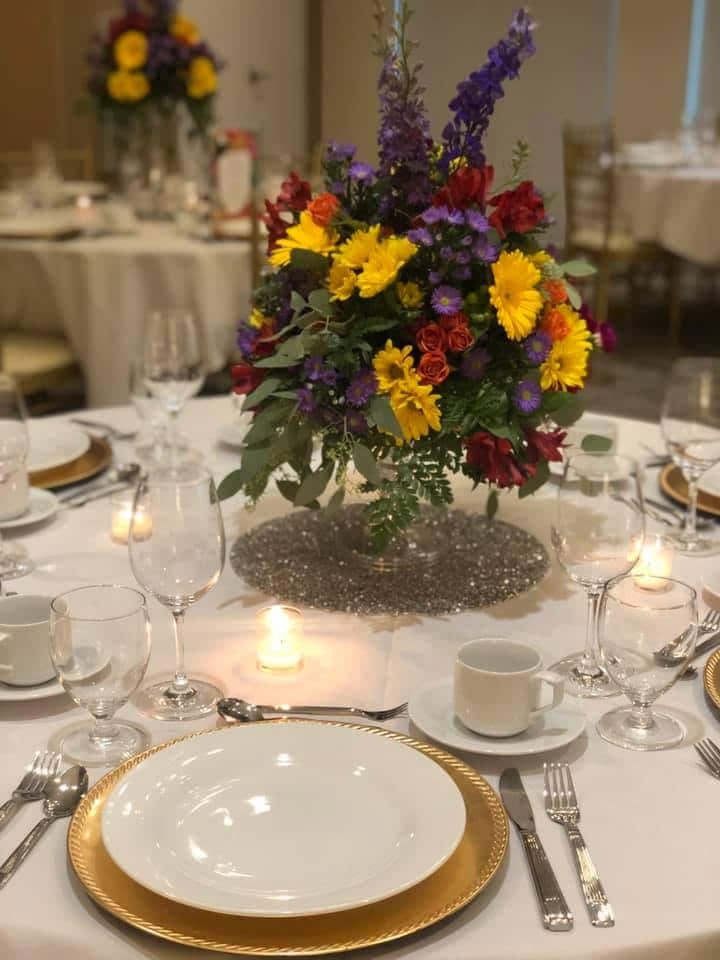 wedding reception table set with white plates, gold chargers and sunflower centerpiece at the Hilton Garden Inn Apopka City Center