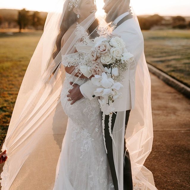 bride and groom wrapped in her veil at sunset holding bouquet of flowers from In Bloom Florist