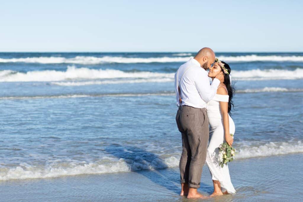 bride and groom standing in shallow water in the ocean by Amy Britton Photography
