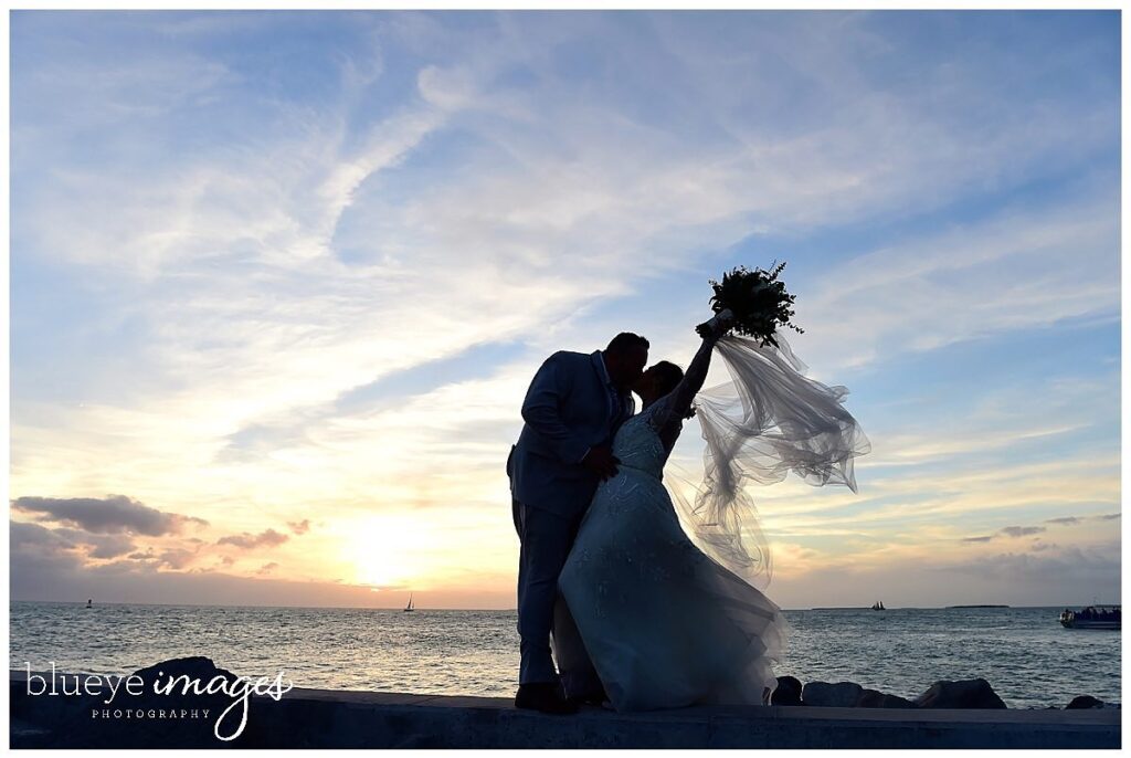 silhouette of bride and groom kissing as the sun sets over the ocean at event planned by Just Save the Date