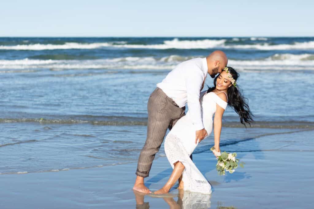 groom dipping his bride toward the ocean by Amy Britton Photography