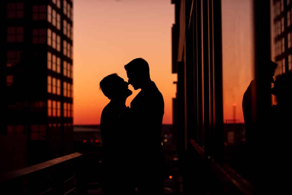 silhouette of grooms kissing against a sunset reflected in a window by Sydney Morman Photography