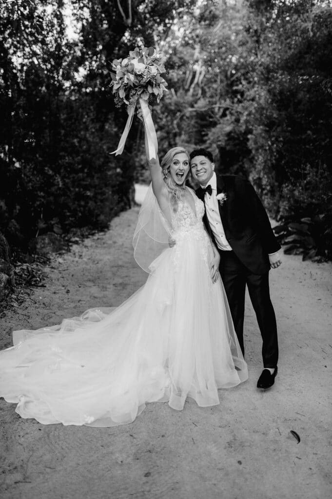 black and white photo of bride holding up her arm in celebration as groom holds her at event planned by Just Save the Date