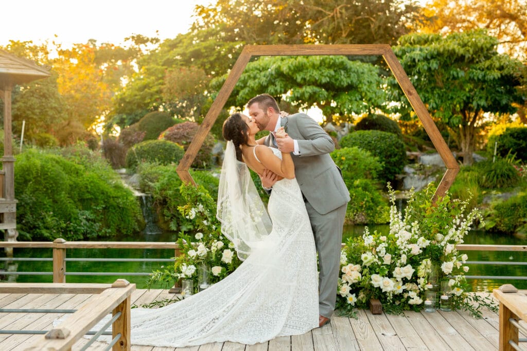 groom dipping and kissing his bride at an outdoor altar of greenery by Sydney Morman Photography