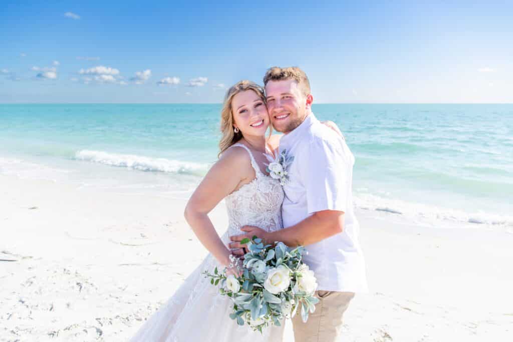 bride and groom posing for a wedding photo with the aquamarine ocean water behind them by Amy Britton Photography