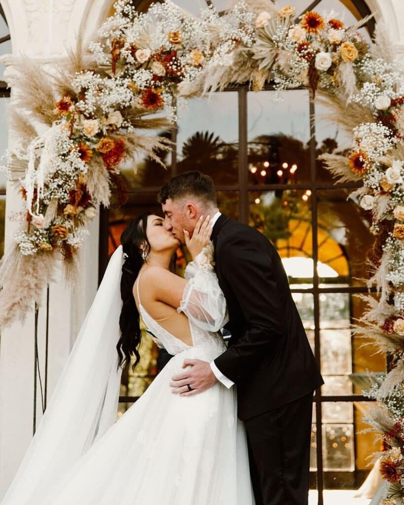 bride and groom kissing under stunning floral arch in neutrals from In Bloom Florist