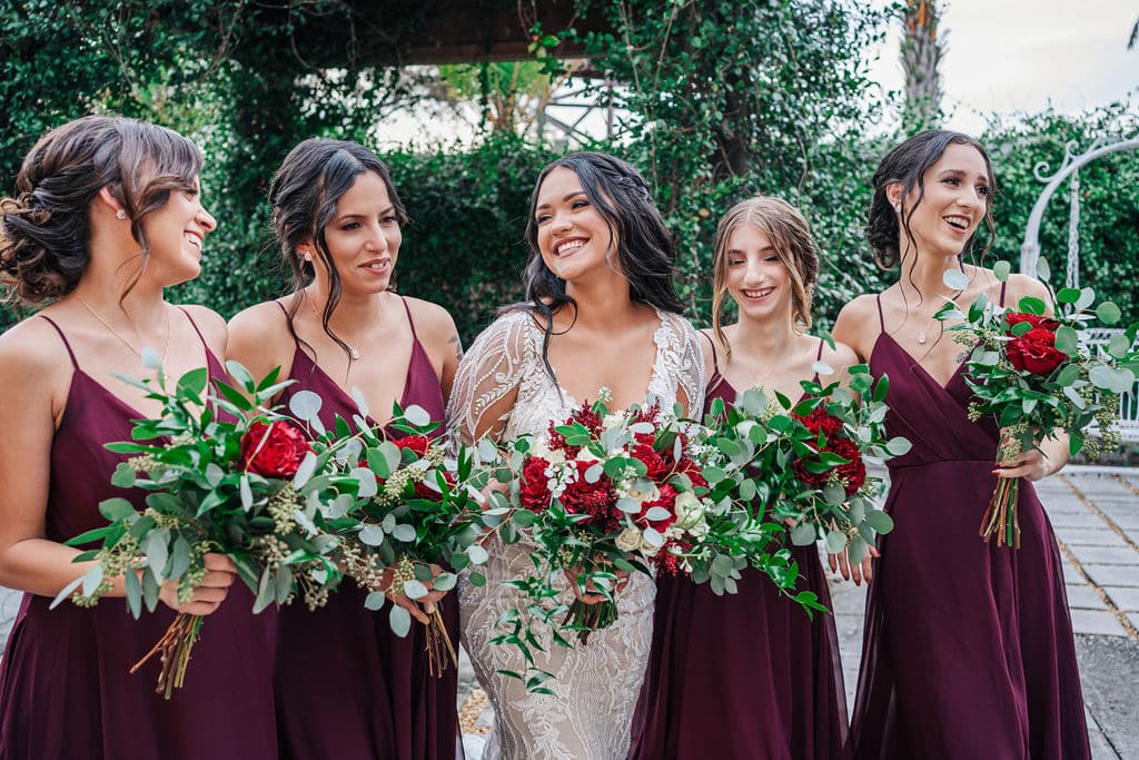 bride posing with bridesmaids in deep red with red rose bouquets