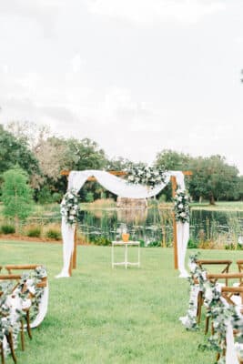 outdoor altar draped with white and greenery along grass path by Making It Matthews