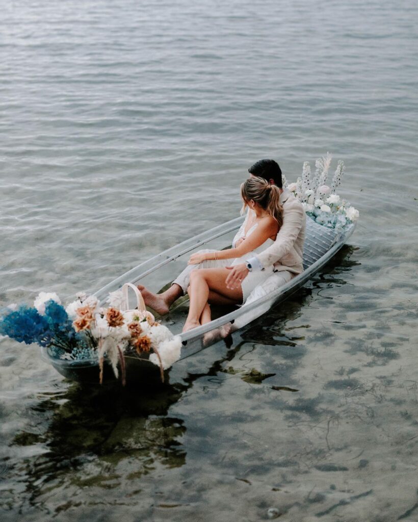 bride and groom floating on glass kayak with blue flowers from In Bloom Florist