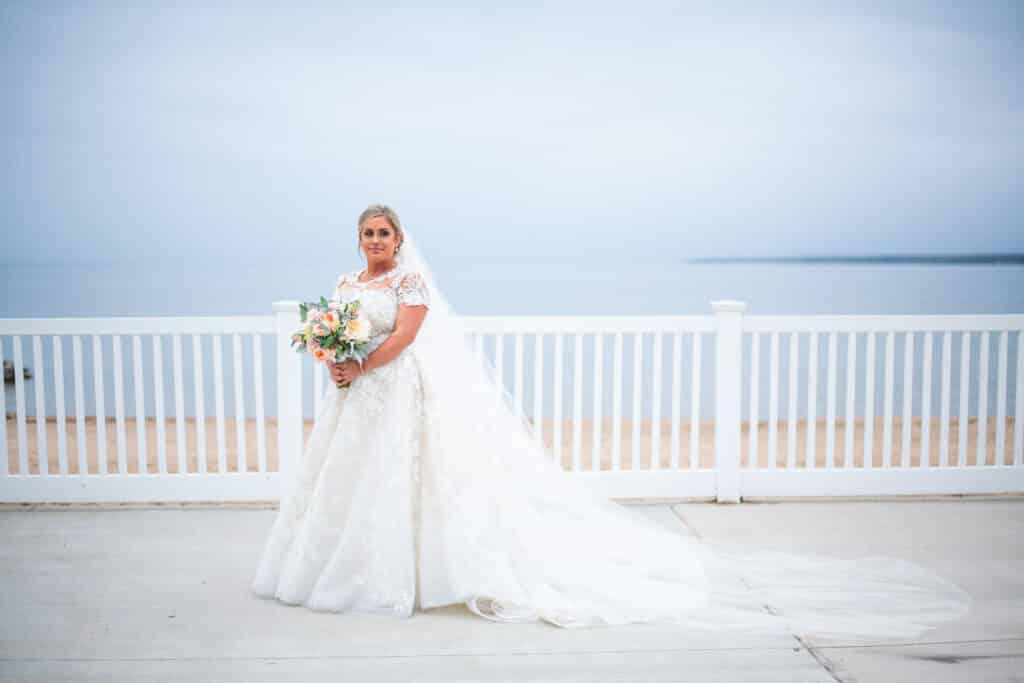 bride posing against a white fence and a blue sky, photo from Weddings By Ray