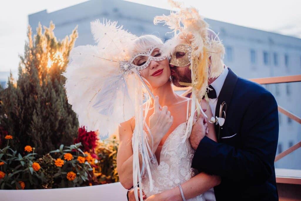 groom kissing his bride with a venetian mask and feathers on, photo from Weddings By Ray