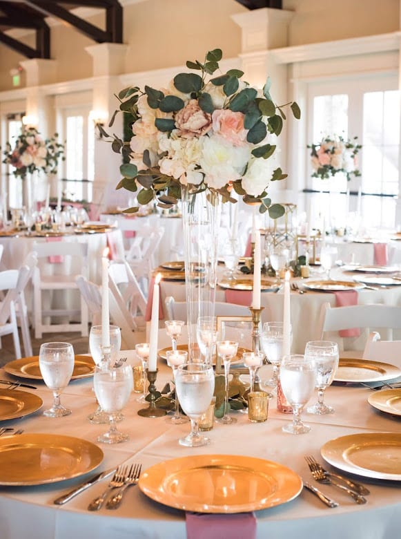 wedding reception guest table set with pink and white tall centerpieces, candles and gold chargers by Making It Matthews