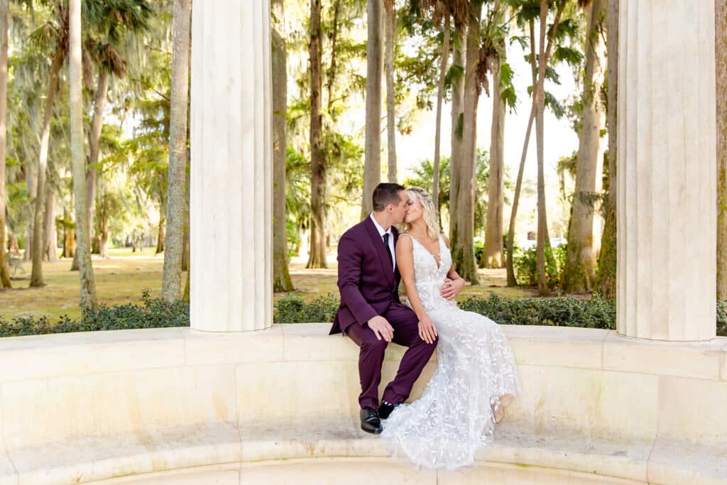 bride and groom sitting in an outdoor rotunda with palm trees in the distance by Amy Britton Photography
