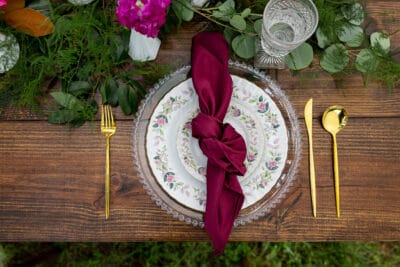 Top view of a floral china set with a maroon tied napkin and gold accents