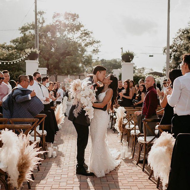 bride and groom kissing in the middle of the aisle as she holds her bouquet from In Bloom Florist