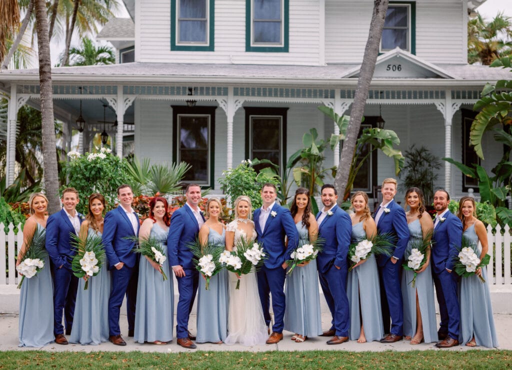 bride and groom in front of old home with groomsmen in blue suits and bridesmaids in complimentary dusty blue at event planned by Just Save the Date