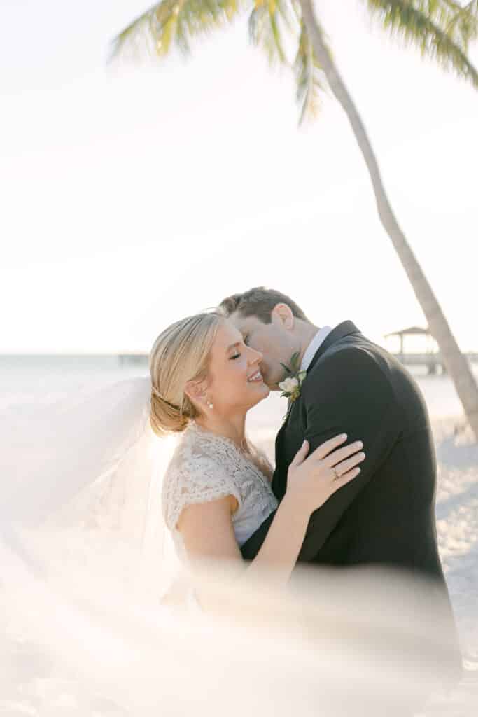 groom kissing bride on the beach under palm tree at event planned by Just Save the Date