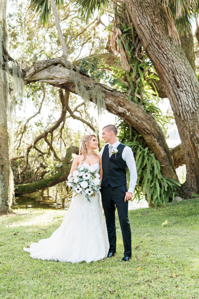 groom and bride with large silk white rose bouquet from Wedding Day Flower Rental standing under oak trees