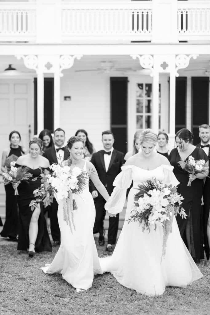 black and white photo of brides smiling and holding hands walking away from event planned by Just Save the Date
