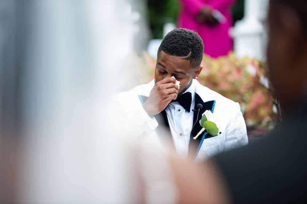 groom wiping his eyes with emotion as he sees his bride walk down the aisle, photo from Weddings By Ray