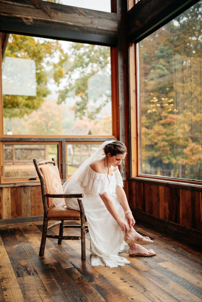 bride sitting on a chair having a quiet moment putting on her shoes photo by Allie & Joey