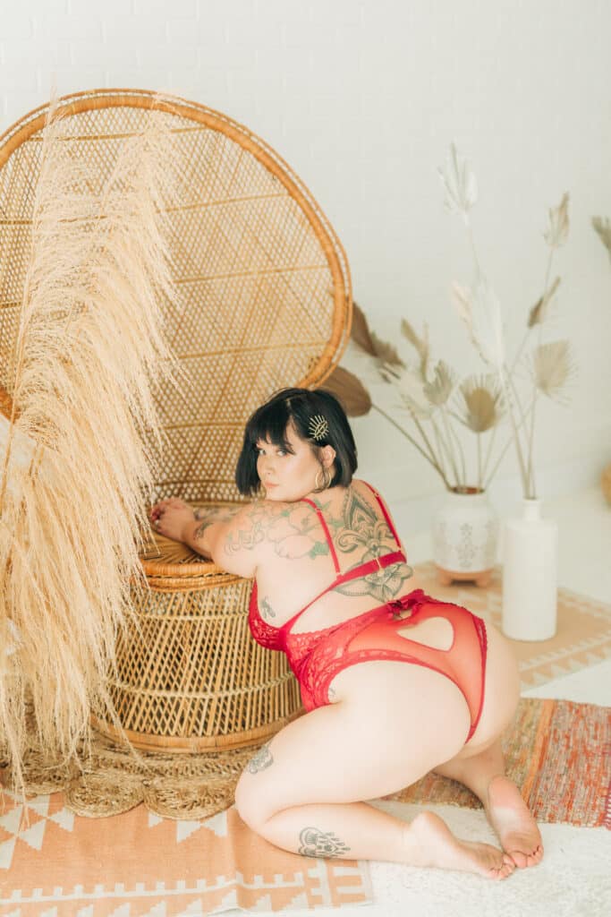 woman in red lingerie kneeling against rattan chair and looking over her shoulder by Sydney Morman Boudoir Photography