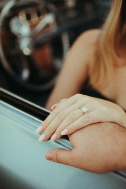 close up image of womans hand resting on top of mans with engagement ring on and pink nail polish