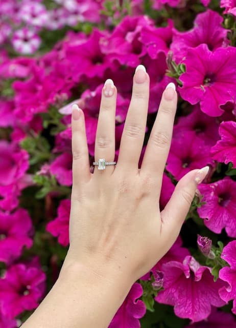 woman's hand held up in front of bright pink flowers with engagement ring on hand