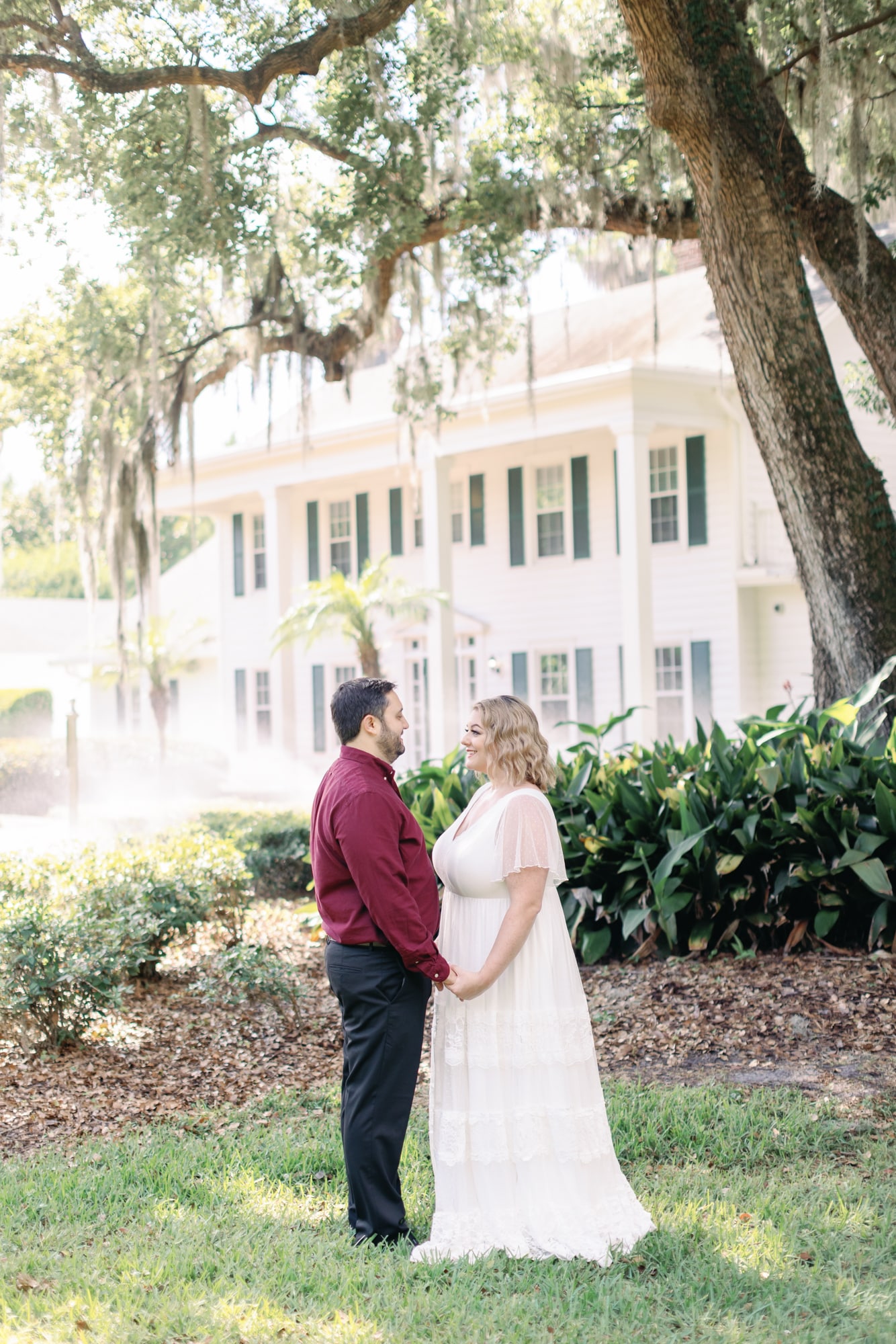 couple stand facing each other together outside in front of estate house under cypress tree