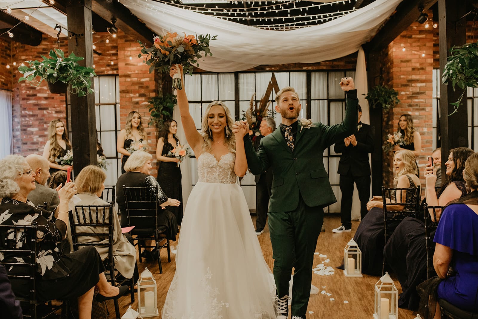 bride and groom walk holding hands with arms up after getting married at ceremony
