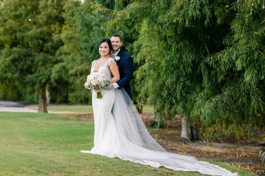 bride and groom pose for photo on a green lawn